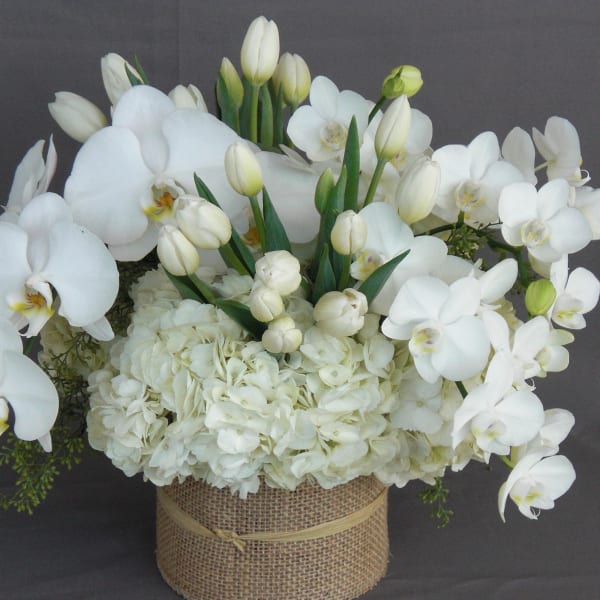 White orchids and hydrangeas arranged in a burlap-wrapped container