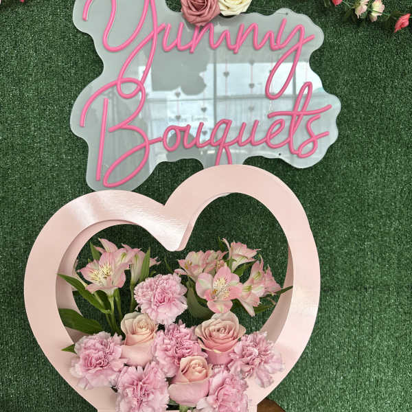 Pink floral arrangement in a heart-shaped box with roses and carnations