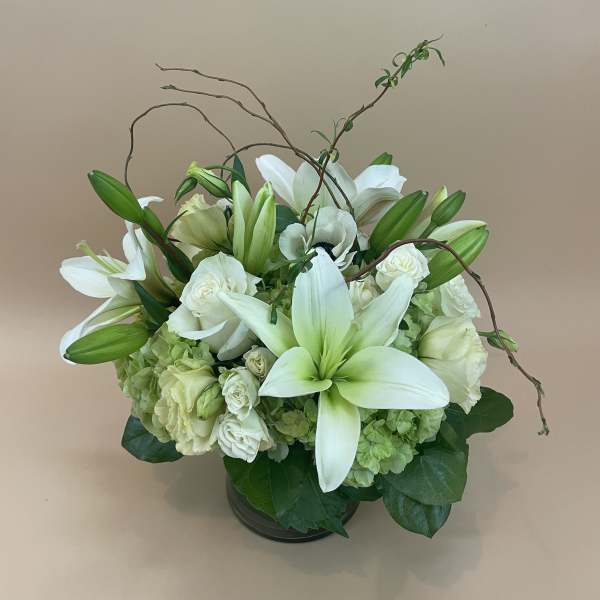 White lilies and roses arranged in a low vase with curved branches