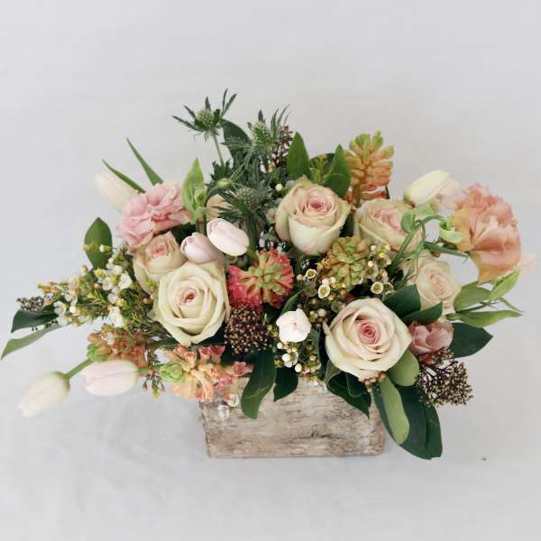 Mixed bouquet of pale roses, tulips, and peach blooms in a rustic wooden container