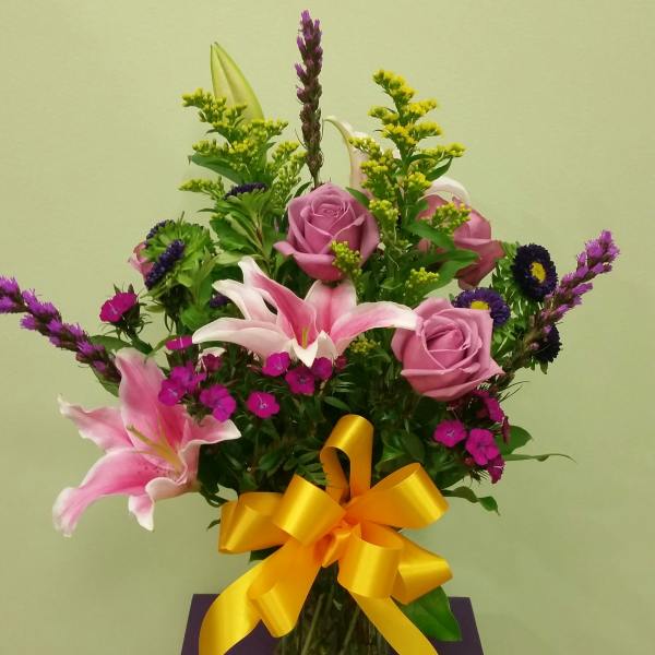 Pink roses and lilies in a glass vase with a yellow ribbon