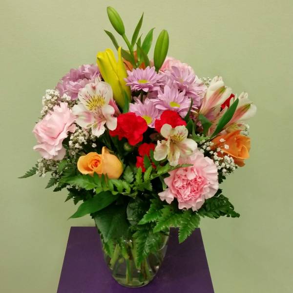 Mixed bouquet of pink, red, yellow, and orange flowers in a glass vase