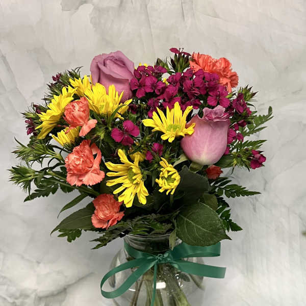 Mixed bouquet of pink roses, yellow daisies, and coral carnations in a glass vase
