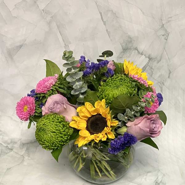Mixed bouquet with sunflowers, pink roses, and green chrysanthemums in a glass vase