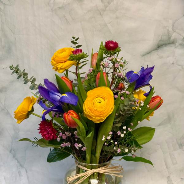 Mixed bouquet in a glass vase with yellow, purple, and coral blooms
