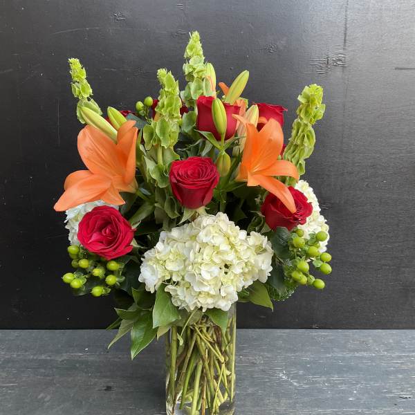 Bouquet of red roses, orange lilies, and white hydrangea in a glass vase