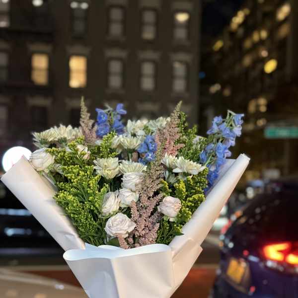 Bouquet of white and blue flowers wrapped in white paper with a yellow ribbon