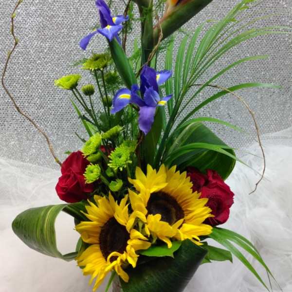 Tropical bouquet with sunflowers, red roses, and bird of paradise in a glass vase