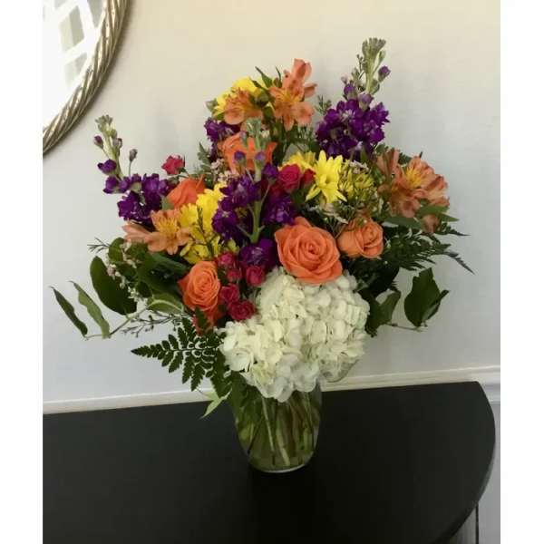 Mixed bouquet of orange, purple, yellow, and white flowers in a clear glass vase