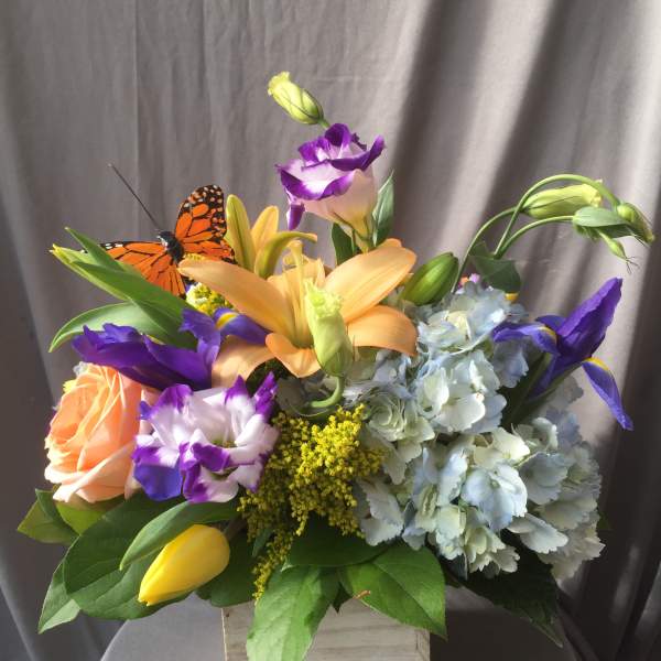 Mixed bouquet with lilies, roses, hydrangea, and a butterfly accent in a wooden box