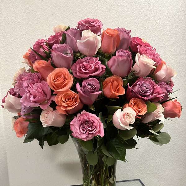 Bouquet of pink, lavender, and coral roses in a clear glass vase