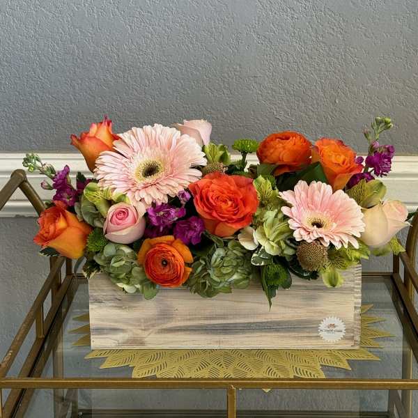 Mixed bouquet of orange, pink, and purple flowers in a wooden box