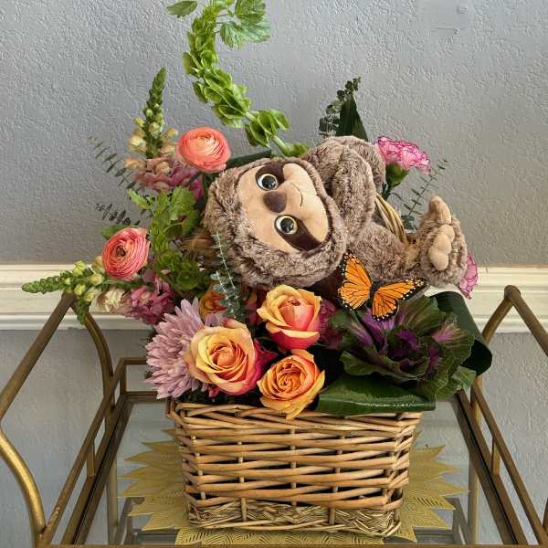 Basket arrangement with roses, mixed flowers, and a plush sloth