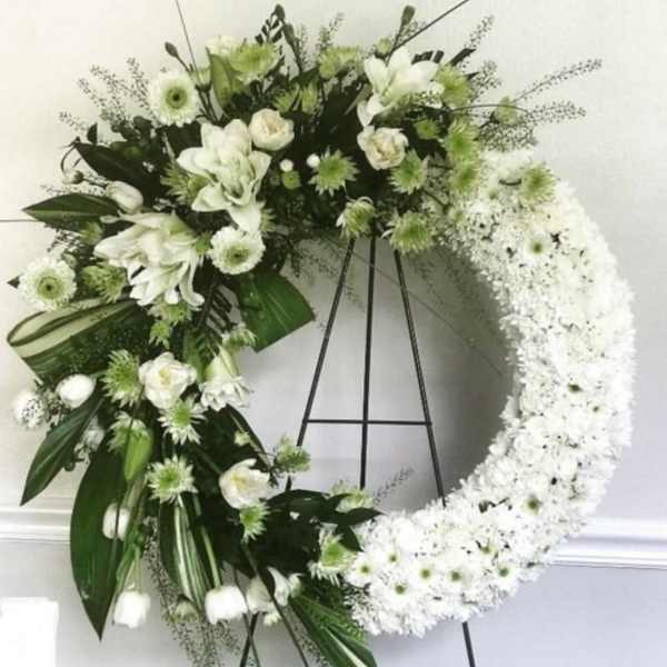 White floral wreath on a black stand with mixed blooms and greenery
