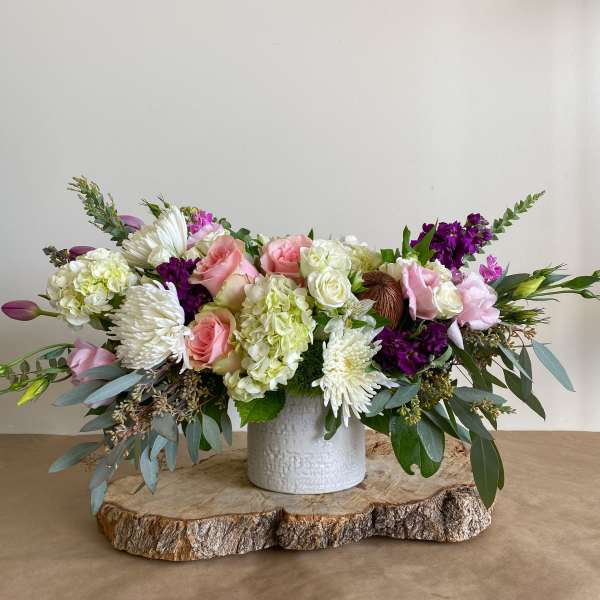 Low floral centerpiece in a white vase with pink, white, and purple blooms