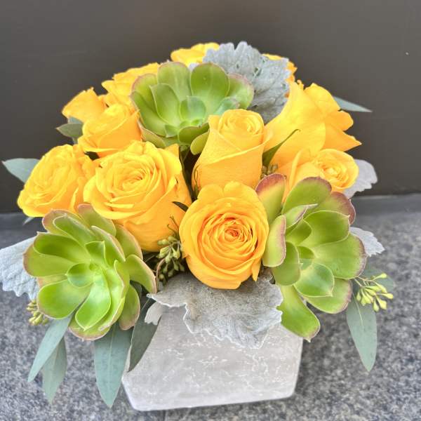 Yellow roses and green succulents in a white square vase