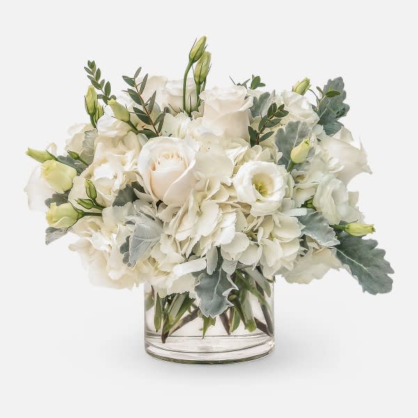 Low arrangement of white roses, hydrangeas, and lisianthus in a clear glass cylinder vase