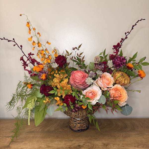 Mixed bouquet in a woven basket vase with roses and orange blooms