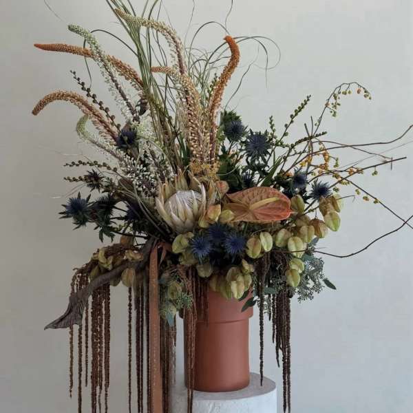 Tall dried floral arrangement in a terracotta vase with trailing elements