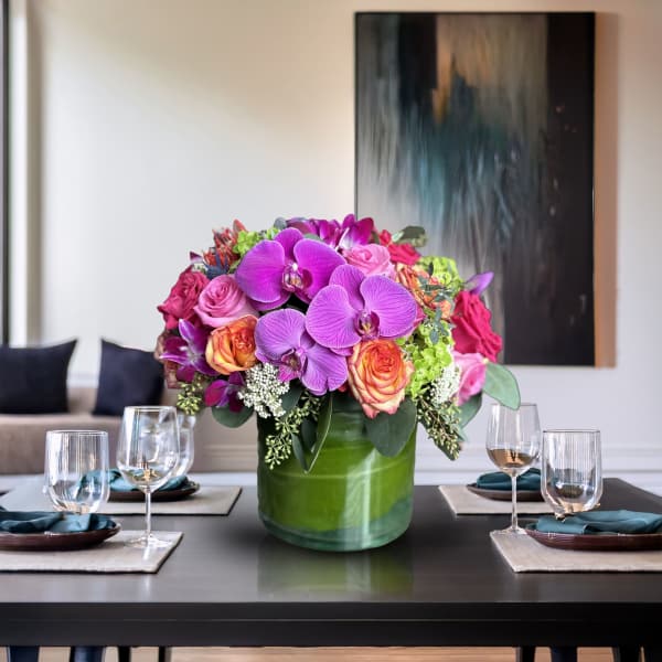 Bright floral centerpiece in a green vase with purple orchids and pink roses