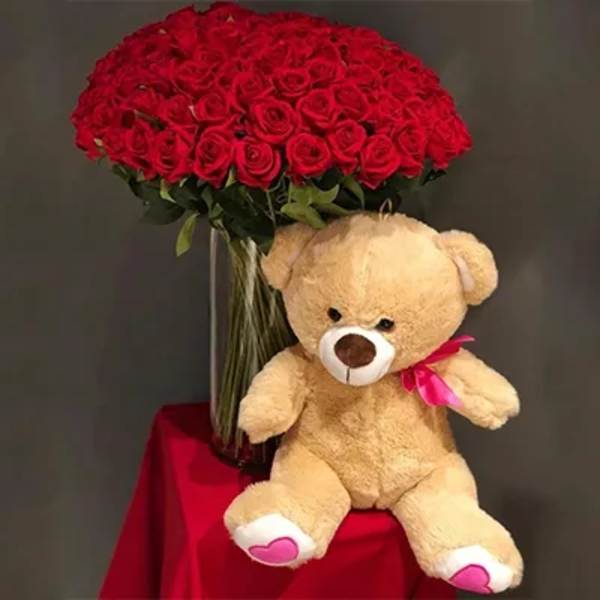Red rose bouquet with a teddy bear sitting beside it