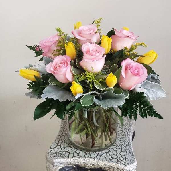 Pink roses and yellow tulips arranged in a clear glass vase