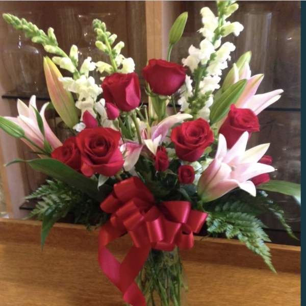 Bouquet of red roses and pink lilies in a glass vase with a red ribbon