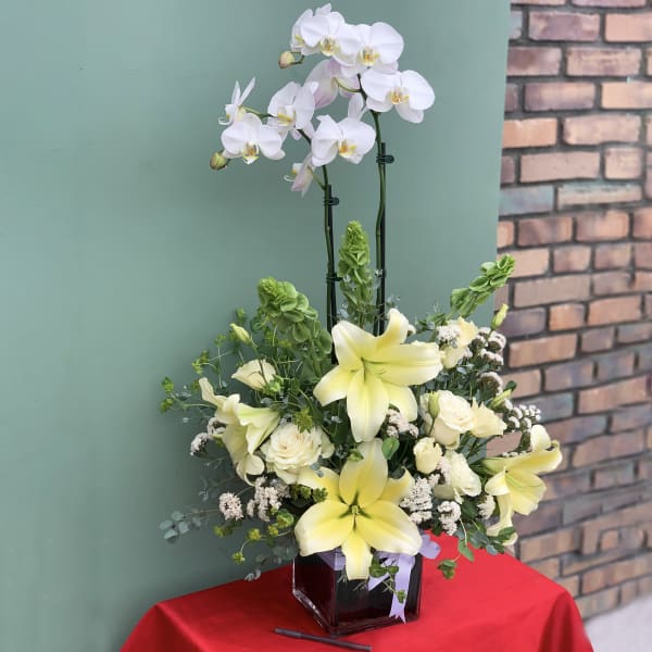 White orchids and pale yellow lilies in a square glass vase