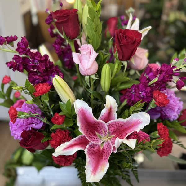 Bouquet of pink lilies, red roses, and purple flowers in a glass vase