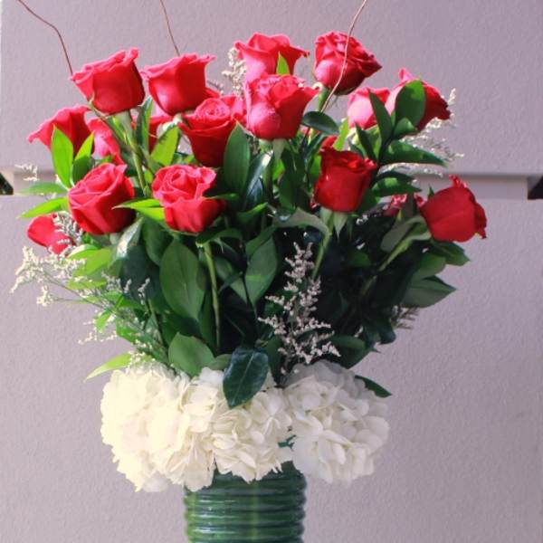 Red roses arranged in a tall green vase with white flowers at the base