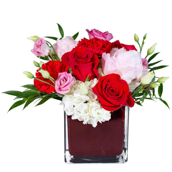 Red and pink flowers arranged in a square glass vase