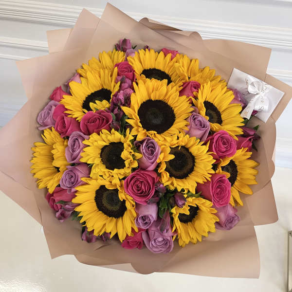 Bouquet of yellow sunflowers and pink-purple roses wrapped in blush paper