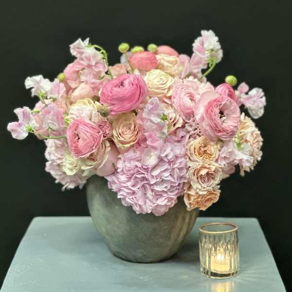 Pink and cream floral arrangement in a gray vase beside a small candle holder
