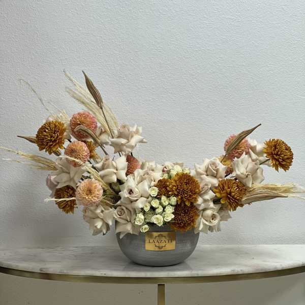 Low floral arrangement in a gray vase with cream and peach blooms