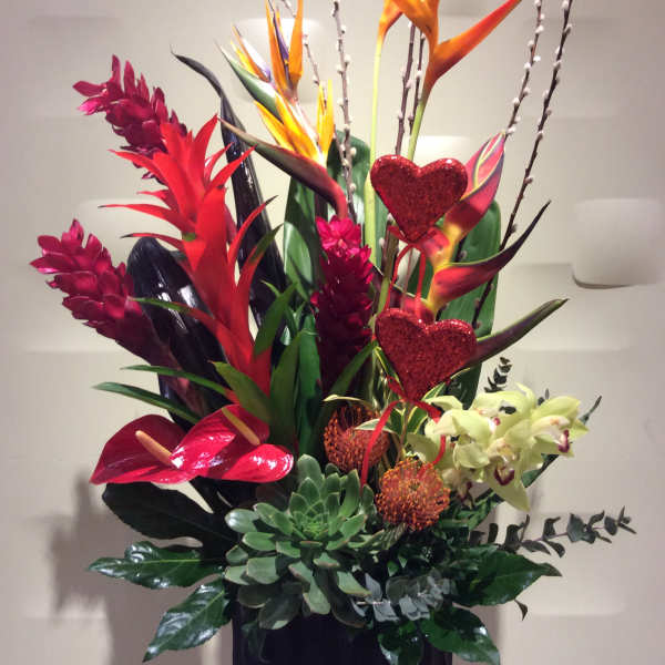Tall tropical arrangement with red and orange blooms in a black container