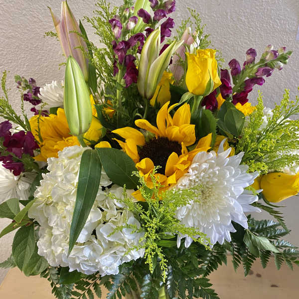 Bouquet of sunflowers, white chrysanthemums, and purple snapdragons in a glass vase