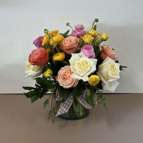 Mixed roses and ranunculus in a glass vase with a plaid ribbon