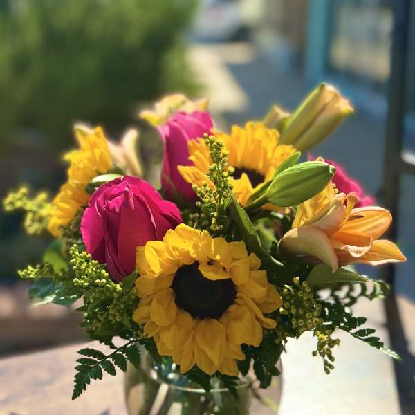 Bouquet of pink roses, yellow sunflowers, and orange lilies in a glass vase