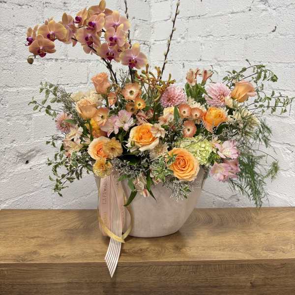 Peach and pink floral arrangement in a beige vase with tall orchid stems