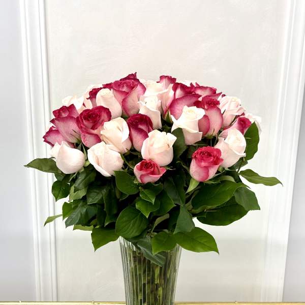Pink and white roses arranged in a tall clear glass vase