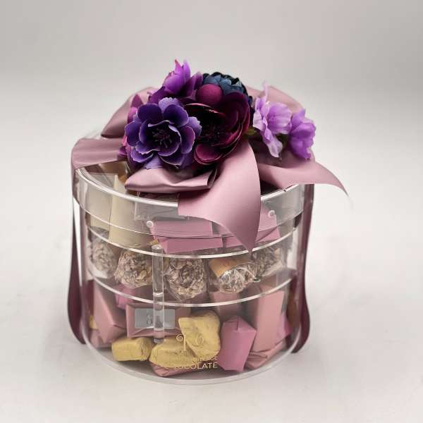 Gift box with purple flowers and chocolates in a clear round container