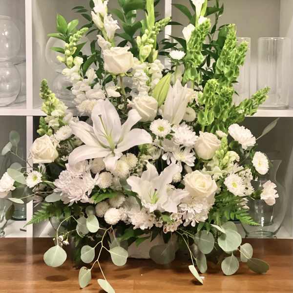 White floral arrangement with lilies, roses, and snapdragons in a low container