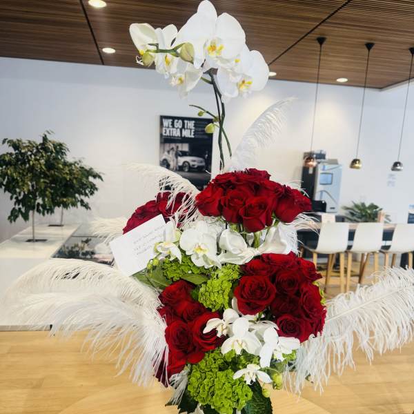 Tall arrangement of red roses and white orchids in a white vase