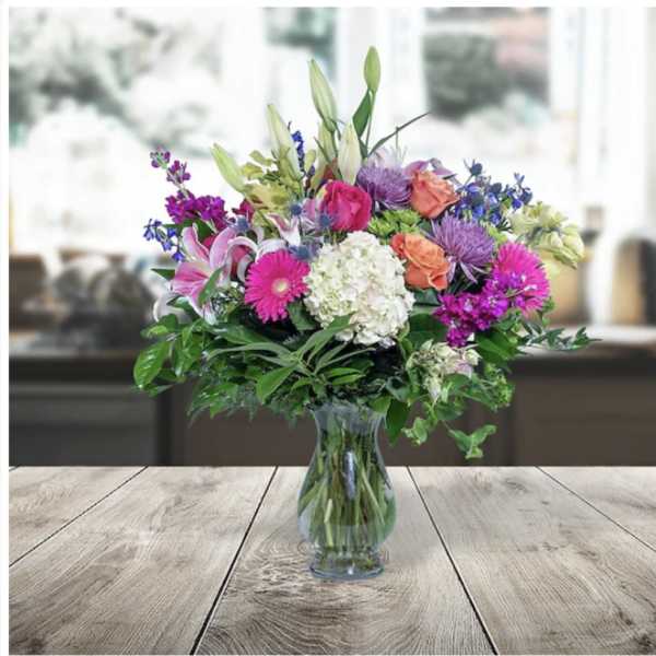 Mixed bouquet of pink, purple, white, and orange flowers in a clear glass vase