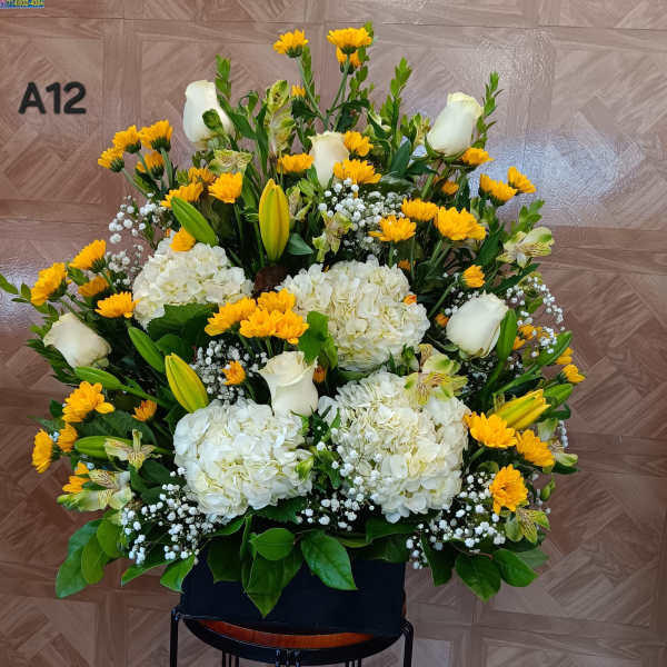 Large floral arrangement with white roses, hydrangeas, and yellow daisies in a black container