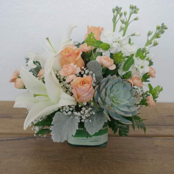 Peach roses and white lilies in a glass vase with a succulent