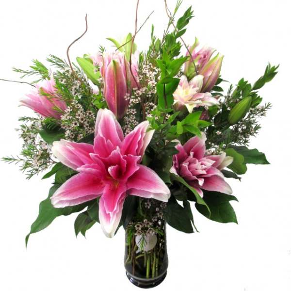 Pink lilies in a glass vase with mixed greenery