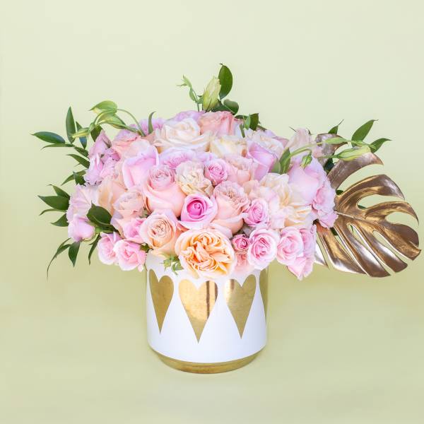 Pink and peach roses arranged in a white vase with gold hearts