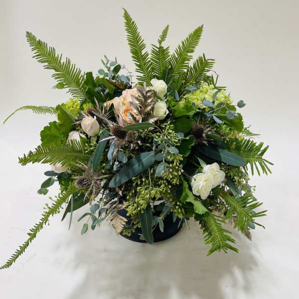 Low floral arrangement with white and peach roses in a dark container