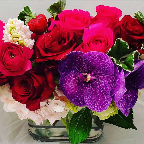 Bouquet of red and pink roses with purple orchids in a glass vase